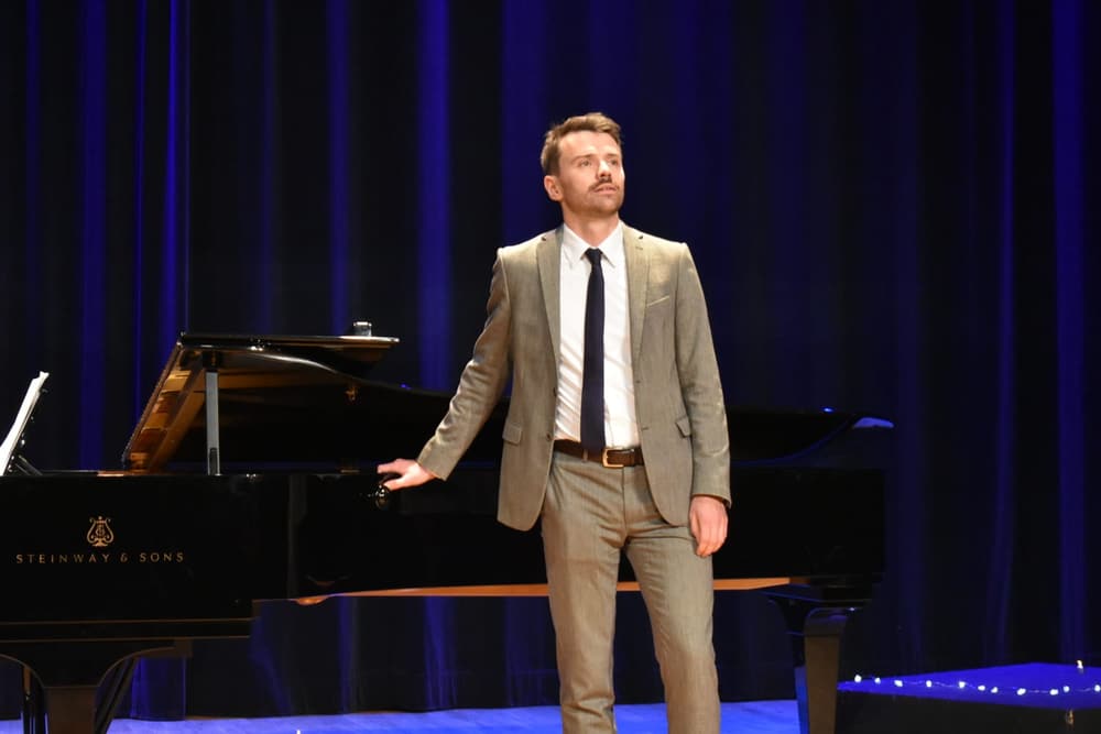 Julien Capy, baryton-basse, en costume sur scène près d'un piano à queue